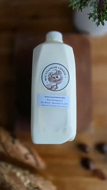 Bottle of local non-homogenized pasteurized whole cow milk with a cream top on a wooden table at Natura Corner