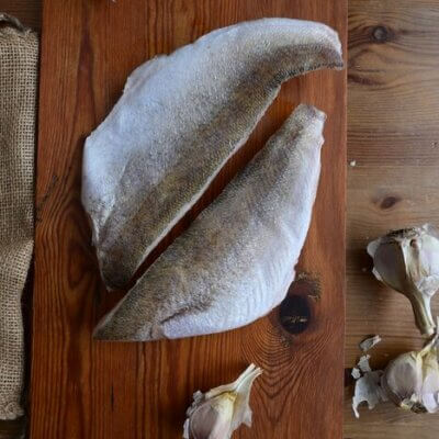 Two boneless wild-caught Lake Erie pickerel fillets on a wooden board with garlic at Natura Corner