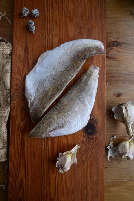 Two boneless wild-caught Lake Erie pickerel fillets on a wooden board with garlic at Natura Corner