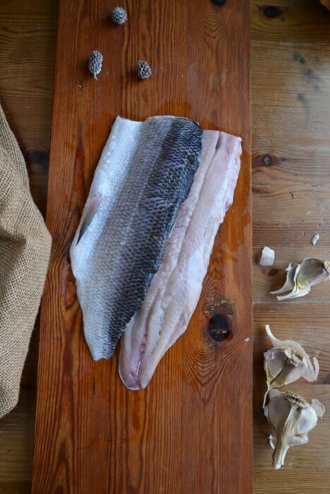 Skin-on wild-caught Great Lakes whitefish fillet on a wooden board with garlic at Natura Corner